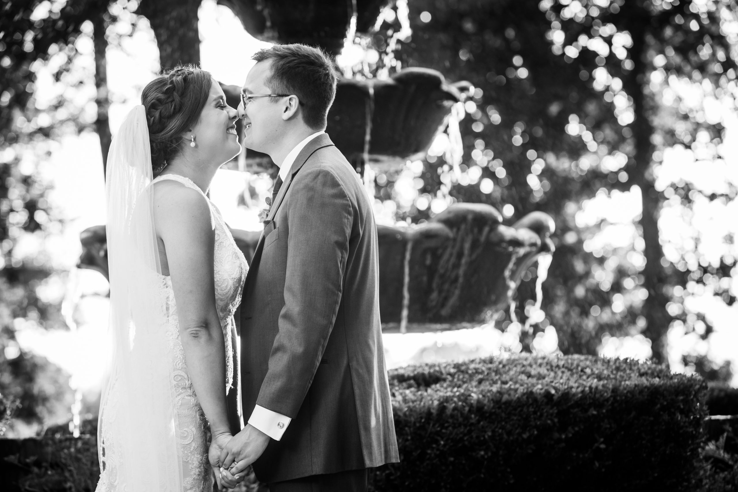 Bride and groom touching noses in front of a fountain