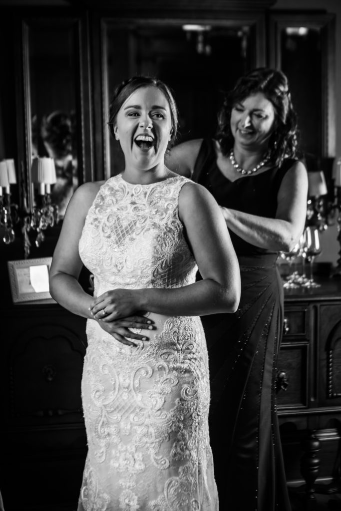 Bride laughing while her mom buttons her dress