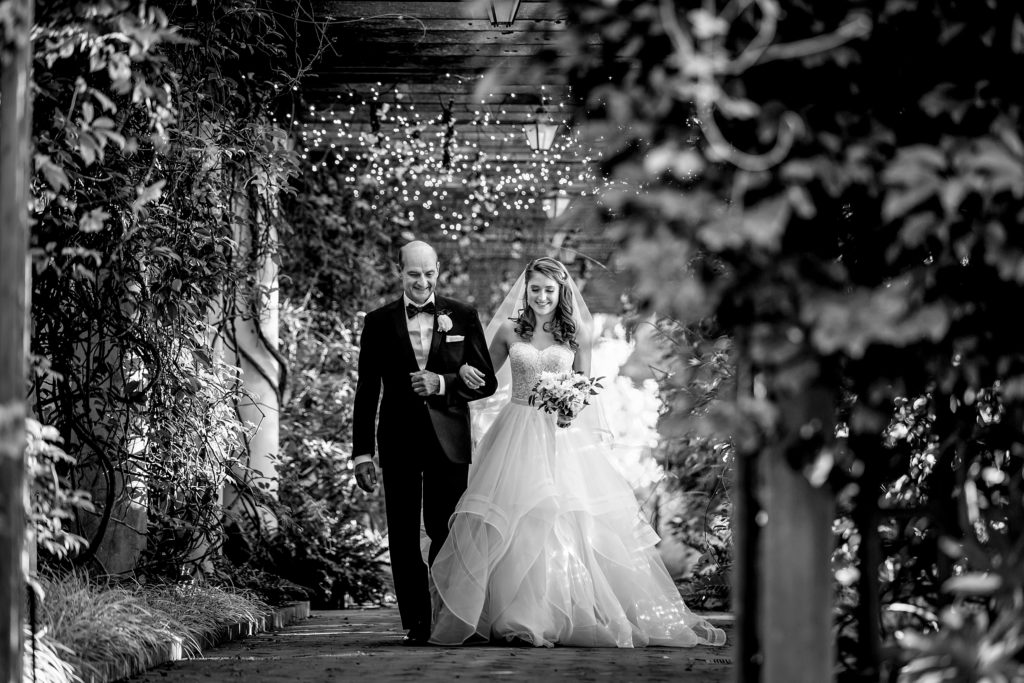 Dad walking his daughter the bride down the isle on her wedding day at Daniel Stowe Botanical Gardens in the White Garden. Greenhouse and garden weddings