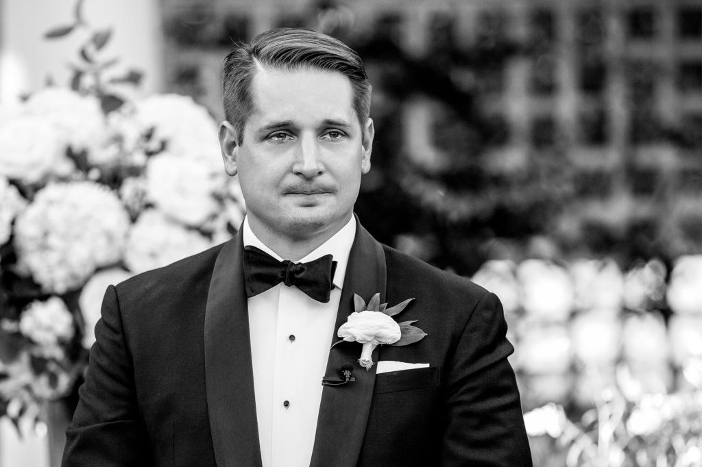 Grooms reaction as he see's his bride walking down the isle for their ceremony at Daniel Stowe Botanical Gardens in the White Garden. Greenhouse and garden weddings
